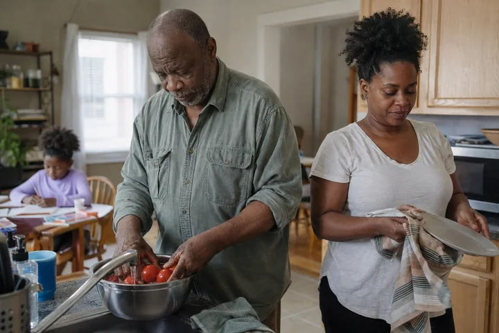 A grandfather and his adult daughter preparing a meal while a child draws at the table